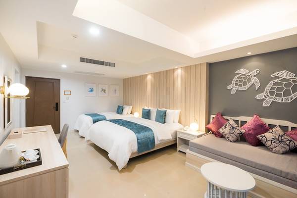 Hotelzimmer im Khao Lak Emerald Beach Resort & Spa mit zwei Betten, Kissen, Dekor und Meerschildkröten an der Wand.