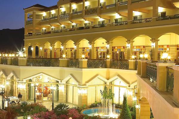 Außenansicht des Lindos Princess Beach Hotels bei Nacht mit beleuchteten Balkonen und Brunnen.