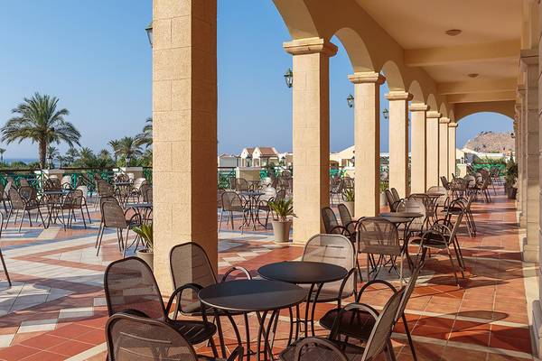 Außenbereich des Lindos Princess Beach Hotels mit vielen Tischen und Stühlen unter Arkaden.