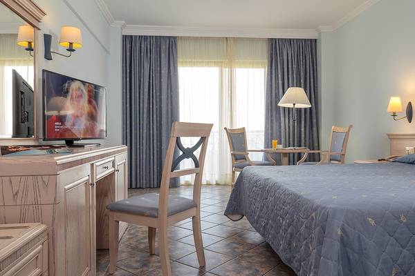 Ein Hotelzimmer im Lindos Princess Beach Hotel mit Bett, Schreibtisch, Fernseher und Möbeln.
