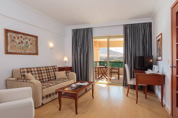 Innenansicht eines Zimmers im Lindos Princess Beach Hotel mit einem Sofa, einem Tisch und einem Fernseher.