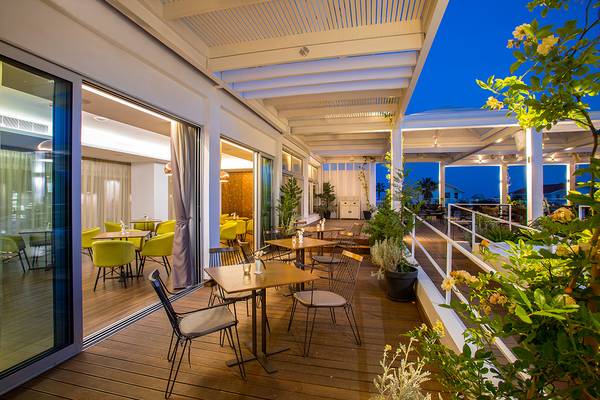 Terrasse des Lordos Beach Hotels mit Tischen und Stühlen, umgeben von Pflanzen und bei Nachtlicht.