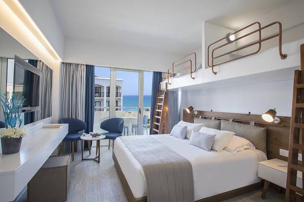 Doppelbett-Zimmer im Lordos Beach Hotel mit Meerblick, zwei Stühle, Tisch, Fernseher und eine Schlafgalerie.