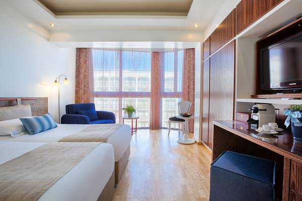 Innenansicht eines Zimmers im Lordos Beach Hotel mit zwei Betten, einem Schreibtisch und einer Aussicht auf die Straße.