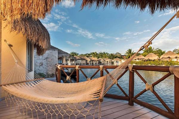 Eine Hängematte auf dem Balkon des Grand Palladium White Sand Resort & Spa mit Blick auf das Wasser und traditionelle Strohdächer.