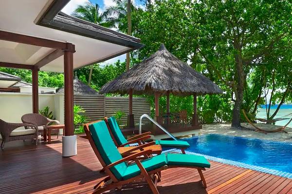 Pool-Terrasse im Coco de Mer & The Black Parrot Suites mit blauem Wasser und grünen Liegestühlen.