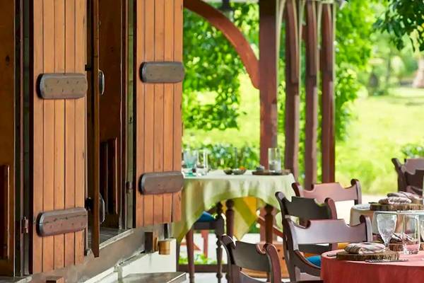 Außenterrasse des Coco de Mer & The Black Parrot Suites mit gedeckten Tischen und Stühlen, umgeben von Bäumen und Gras.