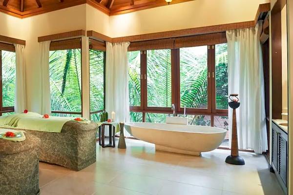 Spa-Behandlungsraum im Coco de Mer & The Black Parrot Suites mit zwei Massageliegen und einer Badewanne vor großen Fenstern.