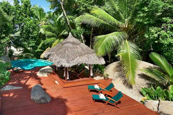 Außenbereich des Coco de Mer Hotels mit Pool, Holzterrasse, Lounge-Stühlen und einer Bambushütte.
