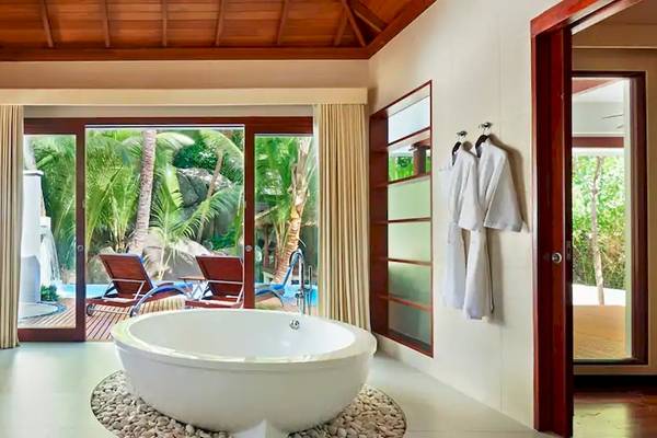 Ein Badezimmer der Coco de Mer & The Black Parrot Suites mit einer Badewanne und einem Ausblick auf einen Pool.
