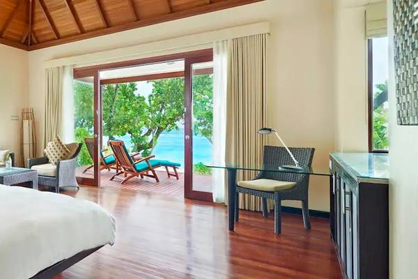 Hotelzimmer mit Meerblick im Coco de Mer & The Black Parrot Suites, mit großem Bett, Sofa, Tisch, Stühlen und Glastür zum Balkon.