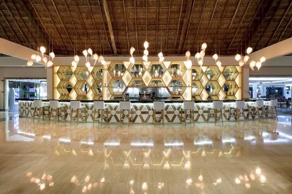 Innenansicht der Bar im Grand Palladium White Sand Resort & Spa mit goldenen Hexagon-Muster und Hängelampen.