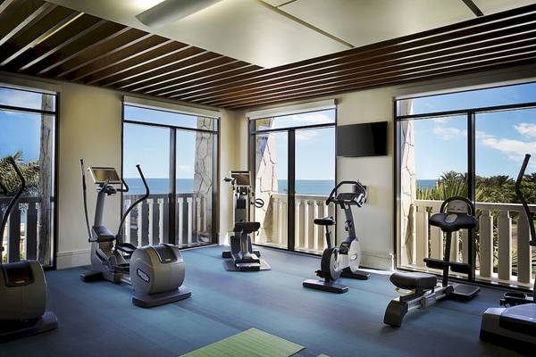 Fitnessraum im Sofitel Dubai The Palm mit Blick auf den Ozean und modernen Geräten.
