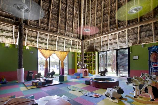 Kinderzimmer im Grand Palladium White Sand Resort mit bunten Teppichfliesen, Spielzeugpferden und einer Spielwiese draußen.