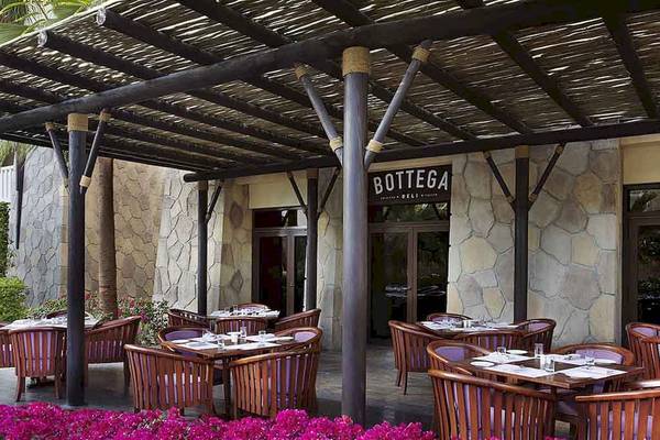 Außenbereich des Restaurants Bottega Deli im Sofitel Dubai The Palm mit holzigen Tischen und Stühlen unter einem Dach.