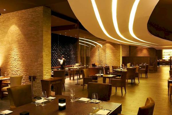 Innenansicht des Restaurants im Sofitel Dubai The Palm mit runden Tischen und Stühlen, warmem Licht und gefliesten Wänden.