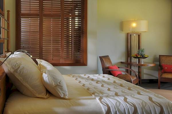 Schlafzimmer im Trou aux Biches Beachcomber Golf Resort & Spa mit einem Bett, Kissen, einem Tisch, Stühlen und einem Badezimmer.
