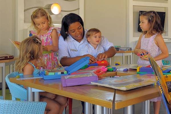 Eine Mitarbeiterin des Trou aux Biches Beachcomber Golf Resort & Spa hilft Kindern beim Basteln an einem Tisch.