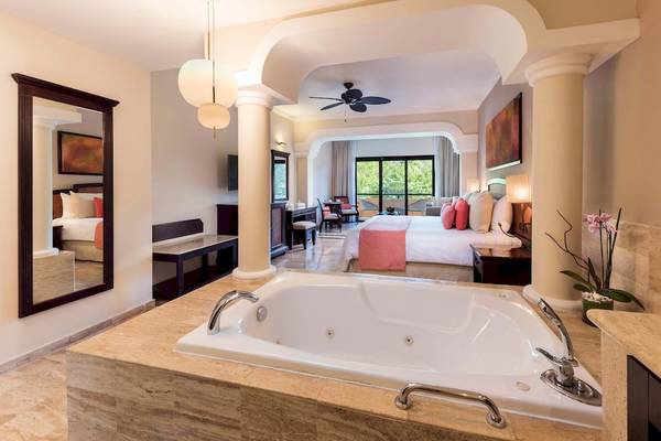 Innenansicht einer Suite im Grand Palladium White Sand Resort & Spa mit Jacuzzi, Bett, Spiegel und Pflanzen.