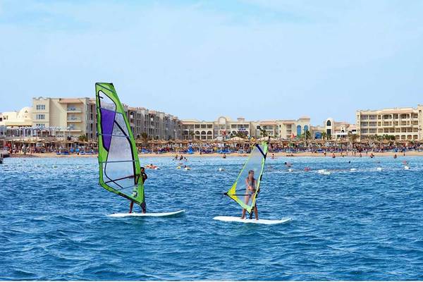 Zwei Personen windsurfen vor dem Pickalbatros White Beach Resort Hotel am Strand.