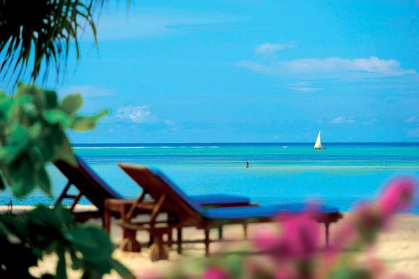 Sonnenliegen am Strand des Neptune Pwani Beach Resort & Spa mit Blick auf das Meer und eine Segelyacht.