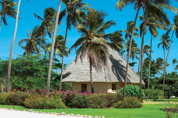 Außenansicht des Neptune Pwani Beach Resort & Spa mit einem kleinen runden Gebäude und umgeben von Palmen und Pflanzen.