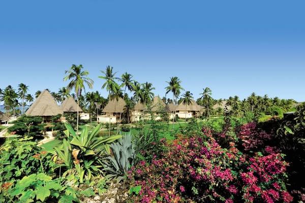 Außenansicht des Neptune Pwani Beach Resort & Spa mit traditionellen Strohhütten und üppiger tropischer Vegetation