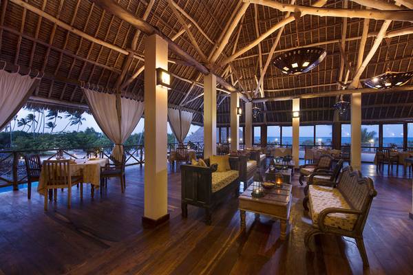 Innenbereich des Neptune Pwani Beach Resort mit Esstischen, Sofas und einer Aussicht auf den Ozean.