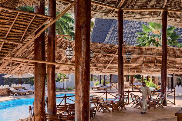 Außenbereich des Neptune Pwani Beach Resort & Spa mit Pool und Holzstühlen.