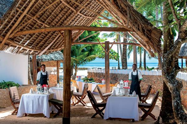 Bedienstete auf der Terrasse des Neptune Pwani Beach Resort & Spa, mit Tischen und Stühlen im Freien.