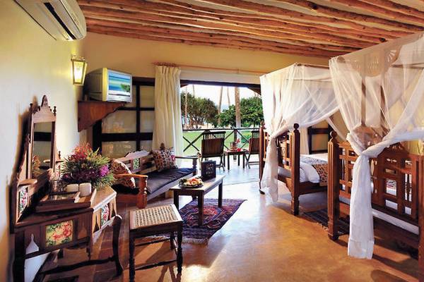Schlafzimmer im Neptune Pwani Beach Resort mit zwei Himmelbetten, Bettwäsche, einem Sofa und einem Fernseher.