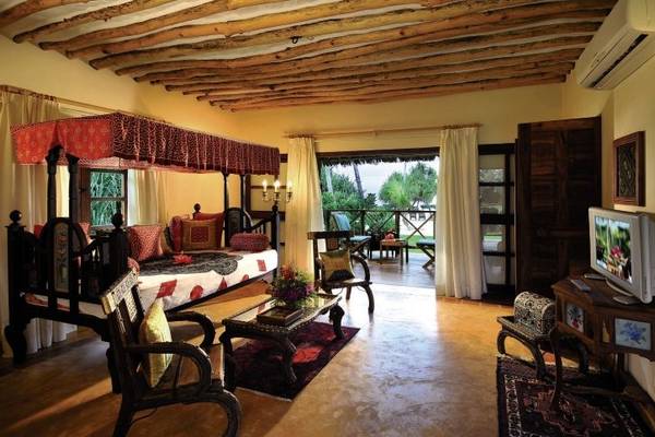 Innenansicht eines Zimmers im Neptune Pwani Beach Resort & Spa mit einem Bett, Möbeln und einem Fernseher.