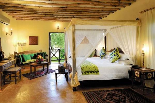 Schlafzimmer im Neptune Pwani Beach Resort mit Himmelbett, Couch, Tisch und Dekoration.