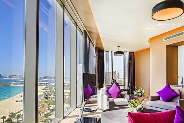 Ein modernes Hotelzimmer mit großer Fensterfront und Blick auf das Meer und die Stadt Dubai.
