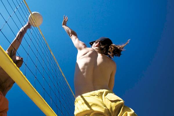 Zwei Männer spielen Volleyball im Freien an einem sonnigen Tag, einer mit einer gelben Cap.