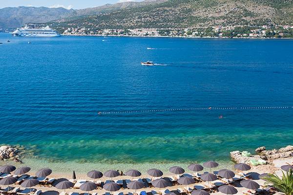 Strand des Club Dubrovnik Sunny Hotel by Valamar mit Sonnenschirmen und Blick auf das Meer.