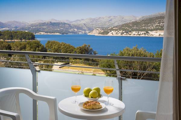 Ein Balkon mit Meerblick im Club Dubrovnik Sunny Hotel mit einem Tisch, zwei Gläsern Orangensaft und einer Platte mit Obst und Croissants.