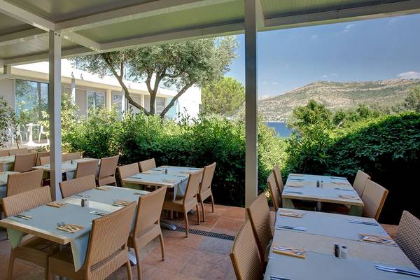 Außenterrasse des Club Dubrovnik Sunny Hotel mit Tischen und Stühlen und Blick aufs Meer.