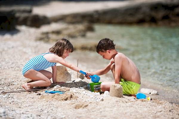 Zwei Kinder bauen eine Sandburg am Strand des Club Dubrovnik Sunny Hotel by Valamar.
