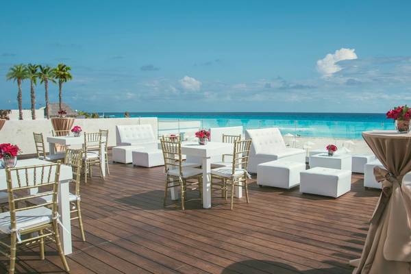 Außenbereich des Coral Level at Iberostar Selection Cancun mit weißen Möbeln und roten Blumen, Blick auf den Strand