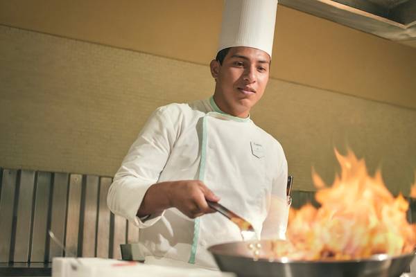 Koch im Coral Level at Iberostar Selection Cancun benutzt ein Wok um Gerichte zuzubereiten