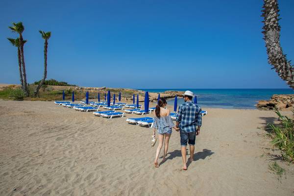 Paar spaziert auf Louis Althea Beach Strand mit blauen Sonnenliegen