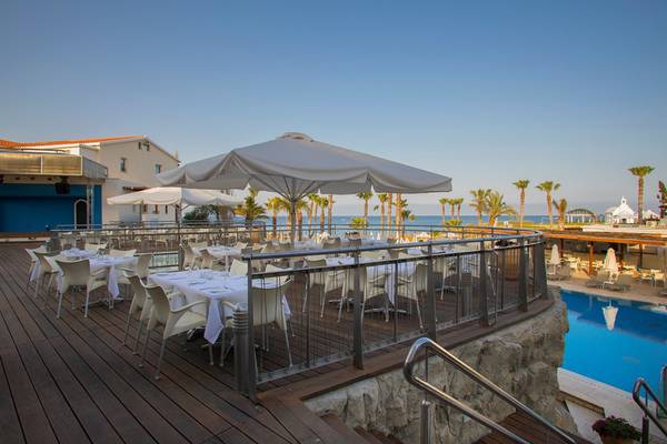 Terrasse des Louis Althea Beach Hotels mit Tischen und Stühlen am Meer.