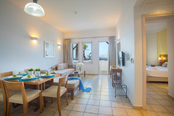 Wohnbereich im Louis Althea Beach Hotel mit Esstisch, Sofa und Fernseher.