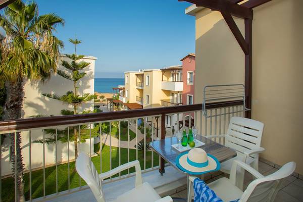 Balkon mit Meerblick im Louis Althea Beach Hotel, mit Tischen, Stühlen und Palmen.