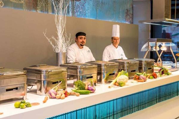 Zwei Köche in der Küche von AX The Palace, das Buffet ist voller Gemüse und Früchte.