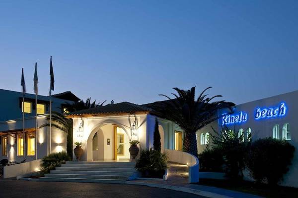 Außenansicht des Mitsis Rinela Beach Hotels bei Nacht mit Beleuchtung und Palmen.