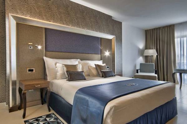 Hotelzimmer im AX The Palace mit einem großen Bett, Kissen, Tischlampe und Sessel.