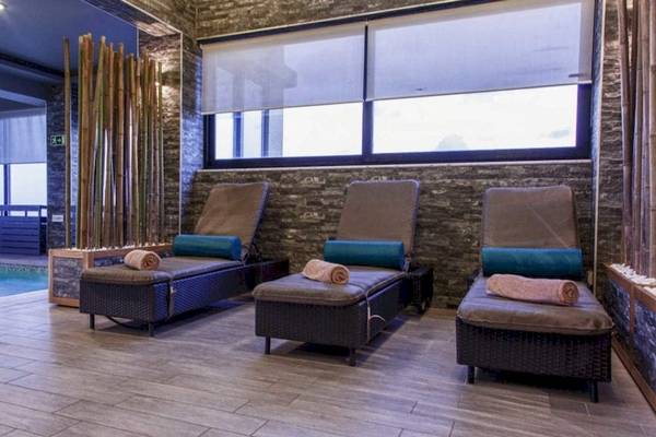 Spa-Lounge-Bereich im AX The Palace Hotel mit drei Liegen, die an einer Wand mit Steinmuster und Glasfenstern ausgerichtet sind.
