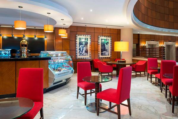 Innenbereich des Sheraton Jumeirah Beach Resorts mit roter Bestuhlung, zentraler Theke und Gemälden an der Wand.